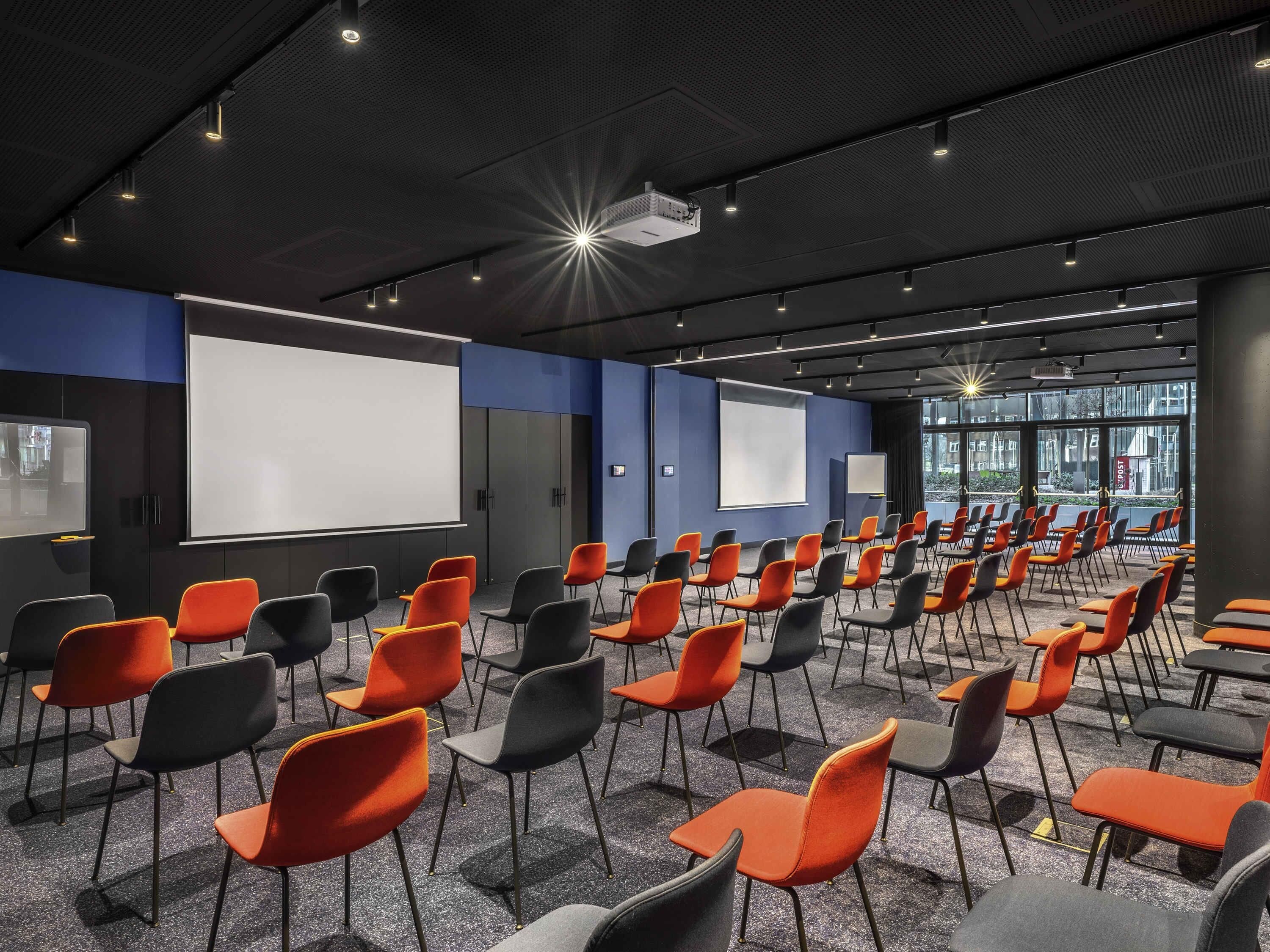 A conference room with rows of chairs, a projector, and a screen.