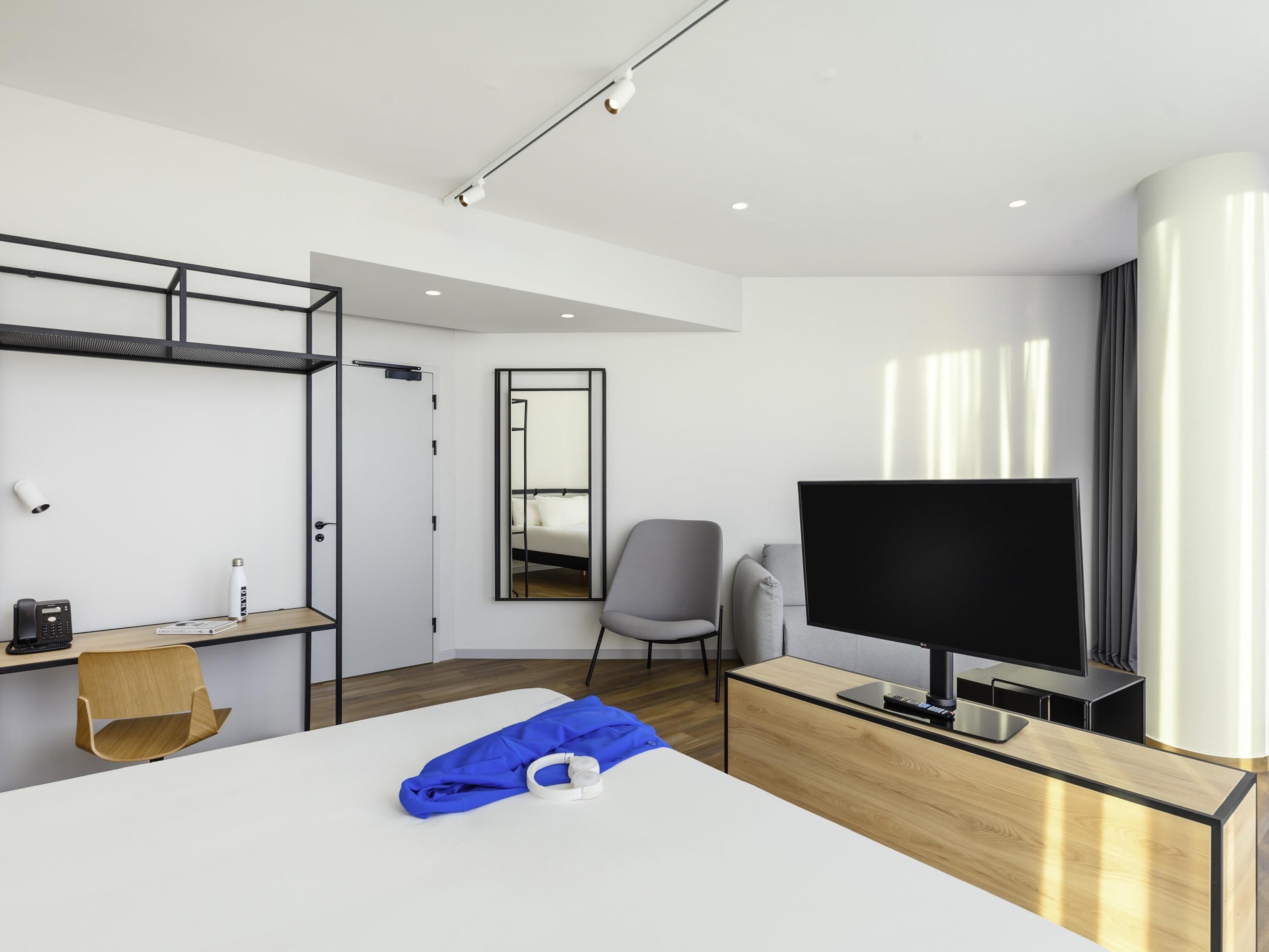 A modern hotel room with a bed, a desk, a chair, a TV, and a large window.