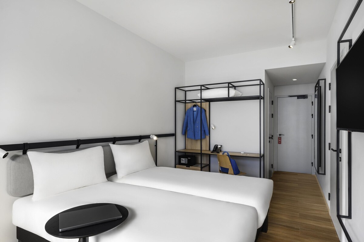 Una habitación de hotel moderna con cama, una mesita pequeña, un armario y un escritorio con silla.