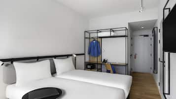 A modern hotel room with a bed, a small table, a wardrobe, and a desk with a chair.