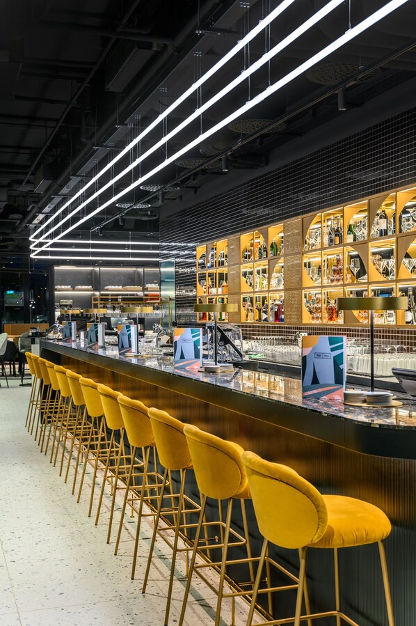 A bar area with yellow bar stools, a long counter, and shelves with bottles and glasses.