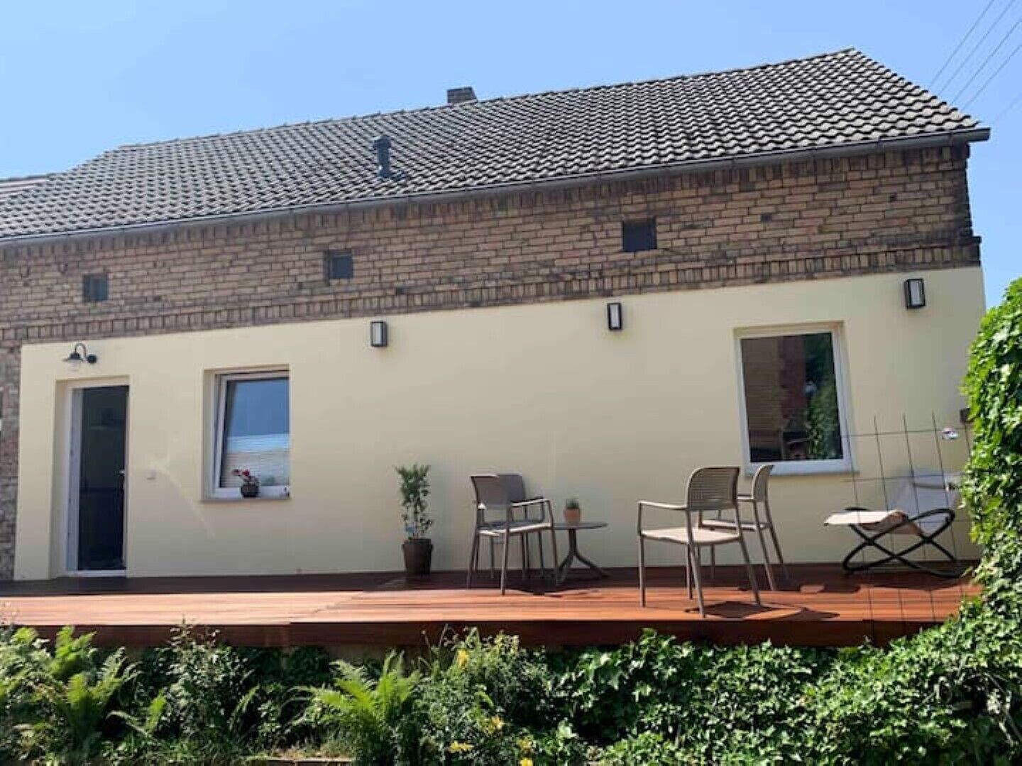 Un bâtiment à deux étages, doté d’un toit recouvert de tuiles, d’un balcon avec des sièges d’extérieur et d’une plante en pot.