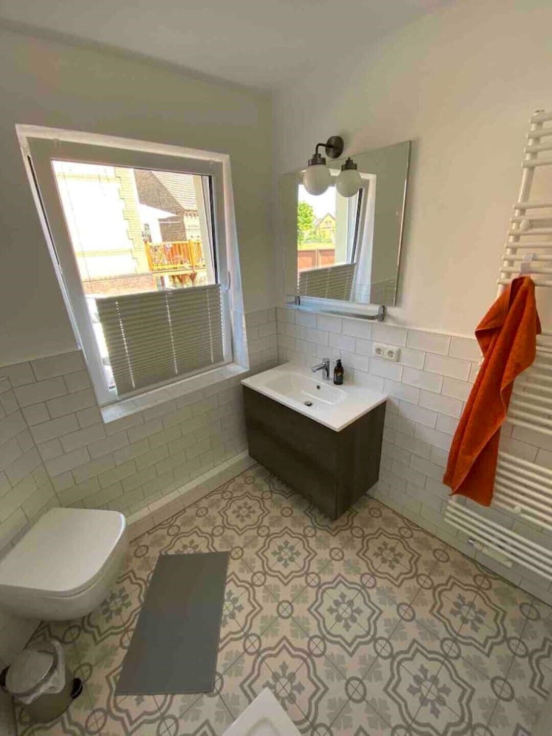 A bathroom with a window, a sink, a toilet, and a shower area.