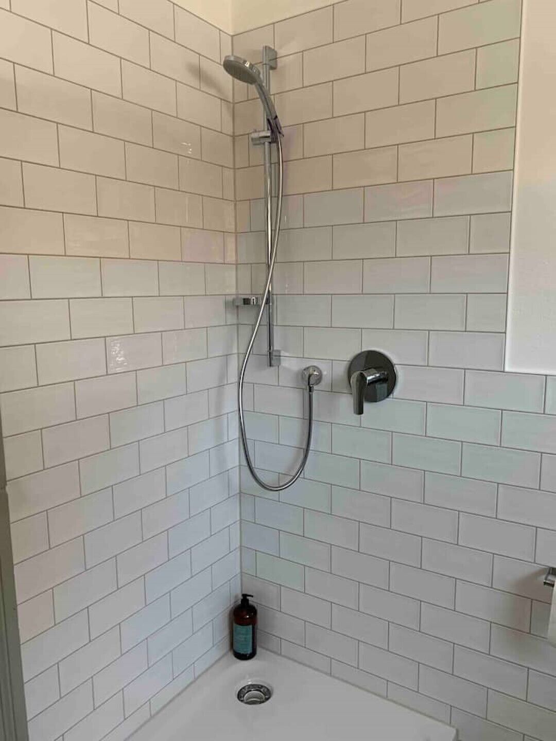 Un espace douche avec des carreaux blancs, une douchette à main et un robinet fixé au mur.