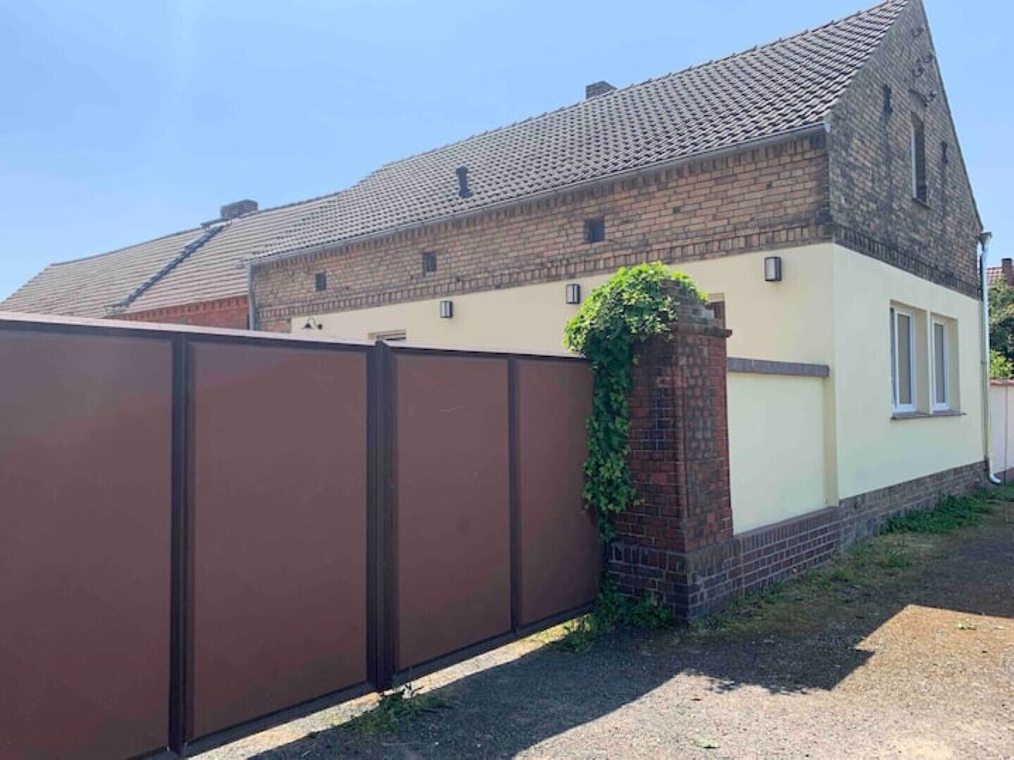 A two-story house with a tiled roof, a brick chimney, and a brown metal fence.