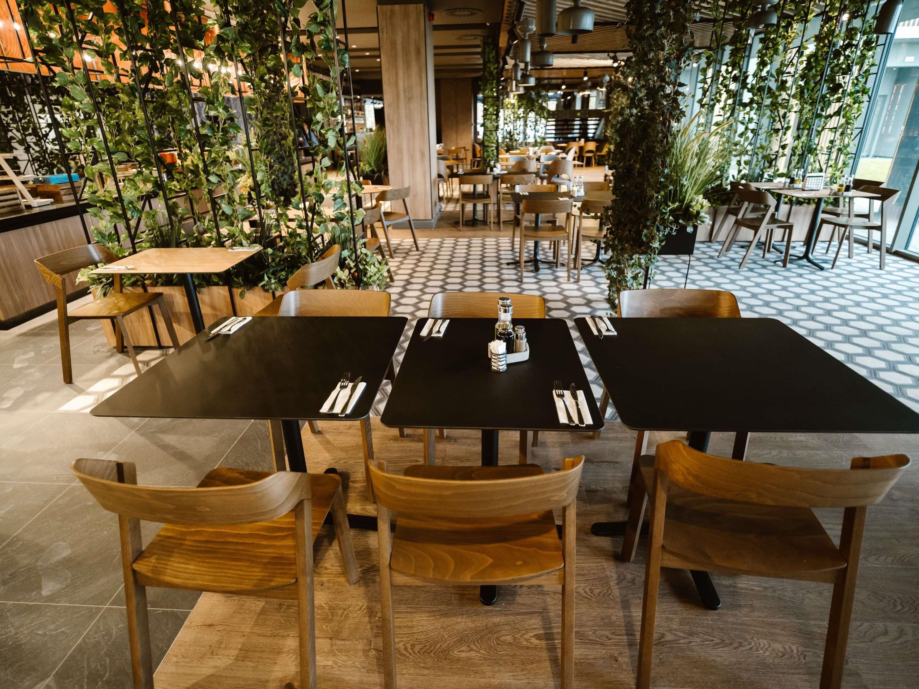 A restaurant with wooden tables and chairs, surrounded by hanging plants.