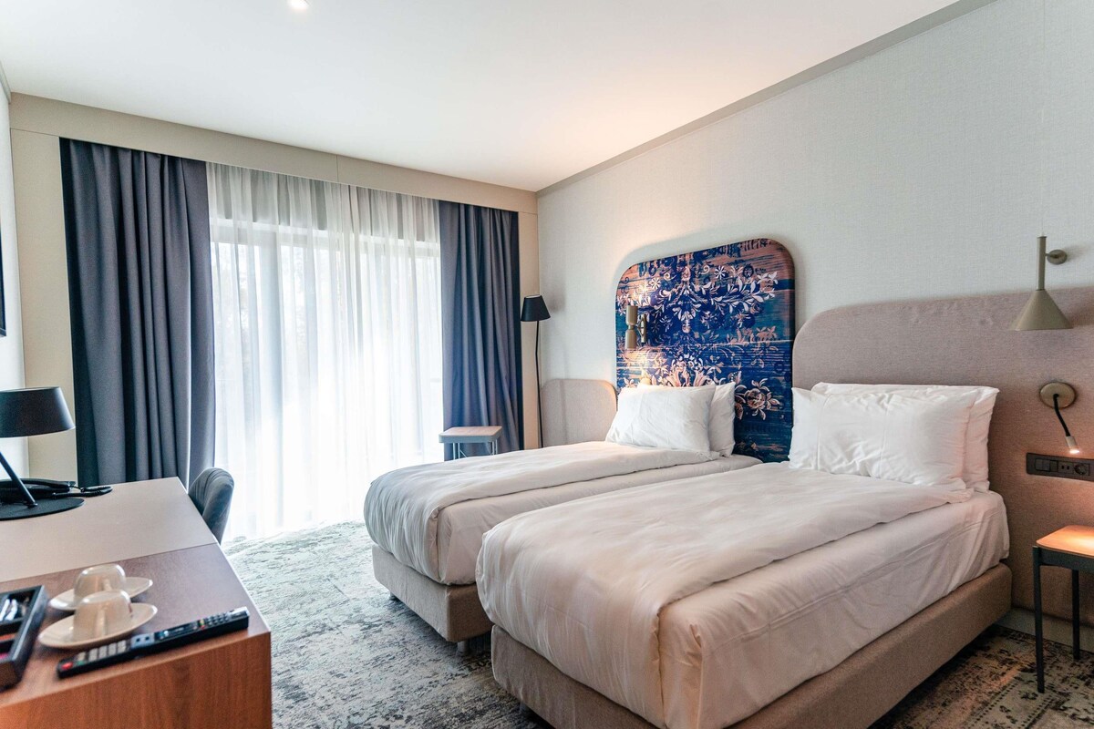Une chambre d’hôtel avec un grand lit, un bureau avec une lampe et une vue sur l’extérieur par la fenêtre.