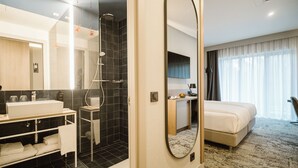 A modern hotel room with a large bed, a separate bathroom with a shower, a vanity with a sink, and a large mirror. - Mercure Sibiu Arsenal (Sibiu)
