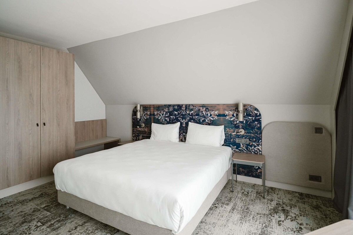 Une chambre à coucher avec un grand lit, une armoire en bois et une tête de lit ornée d’un motif floral.