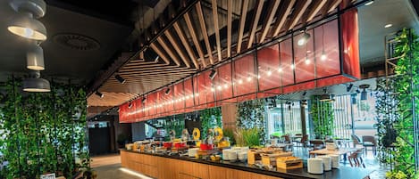 A modern kitchen area with a long counter, various kitchen appliances, and a dining area with tables and chairs.