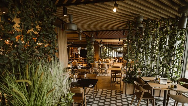 A modern restaurant interior with hexagonal patterned flooring, wooden tables and chairs, hanging plants, and pendant lighting. - Mercure Sibiu Arsenal (Sibiu)
