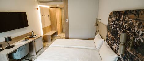 A hotel room with a bed, a desk with a chair, a TV, and a bathroom visible through an open door.