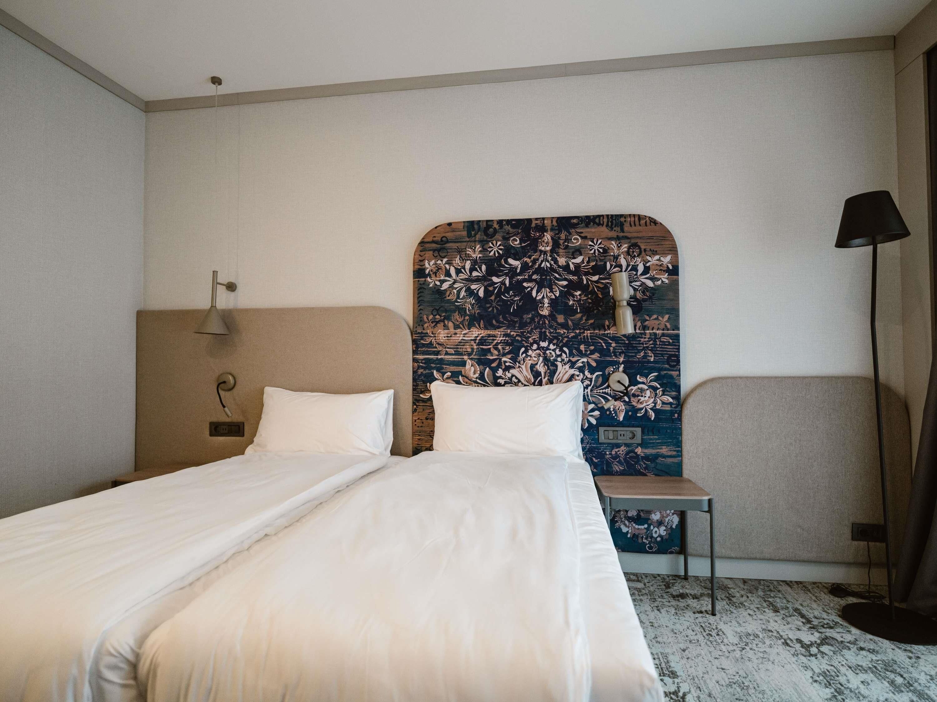 Une chambre d’hôtel avec un grand lit, une petite table, une lampe et une tête de lit décorative.