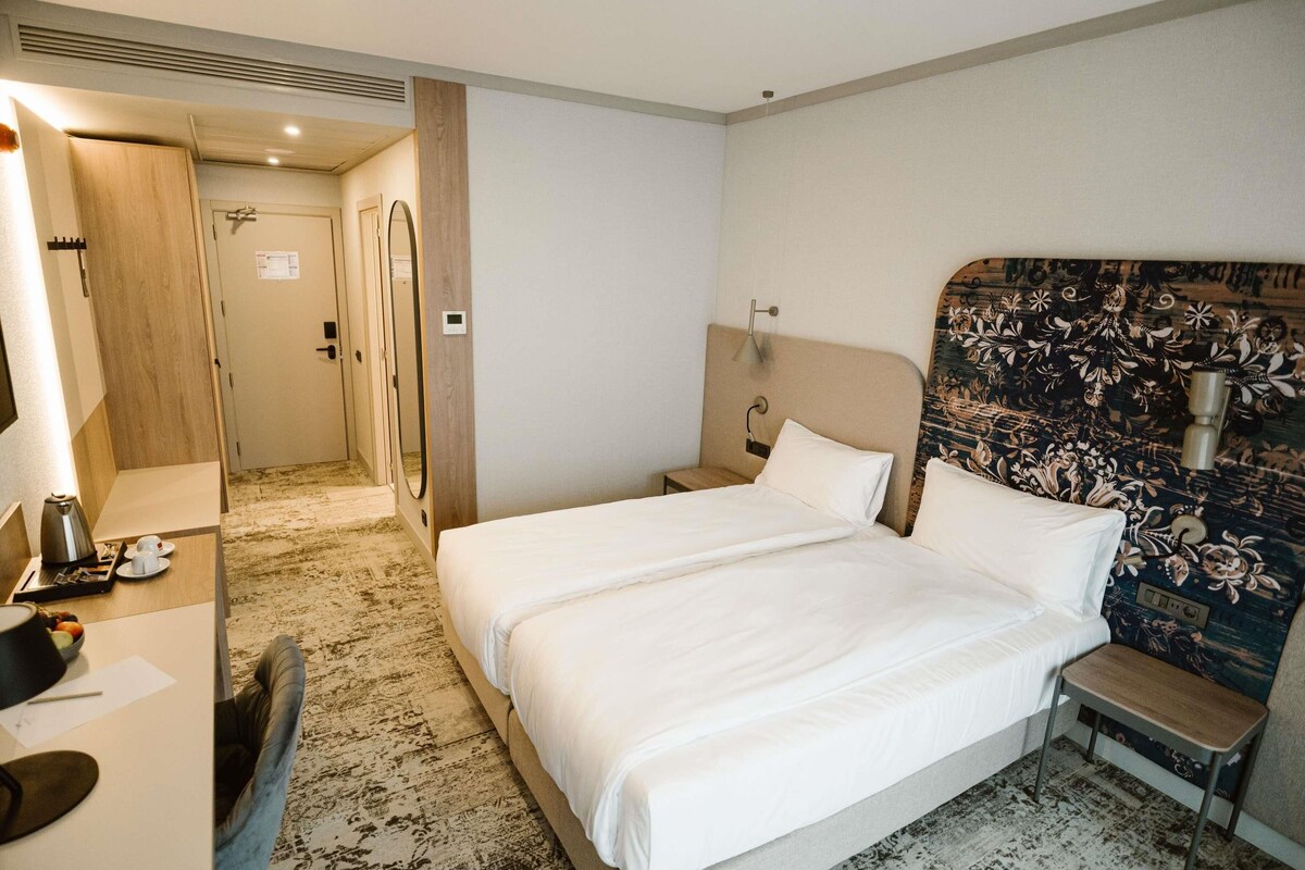 Une chambre d’hôtel avec un grand lit, un bureau avec une chaise, un miroir et un espace douche.