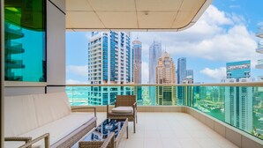 Un balcone con un divano, poltrone in vimini e un tavolo in vetro. Dalla sua posizione si gode una vista sulla città, con grattacieli e un porto turistico.