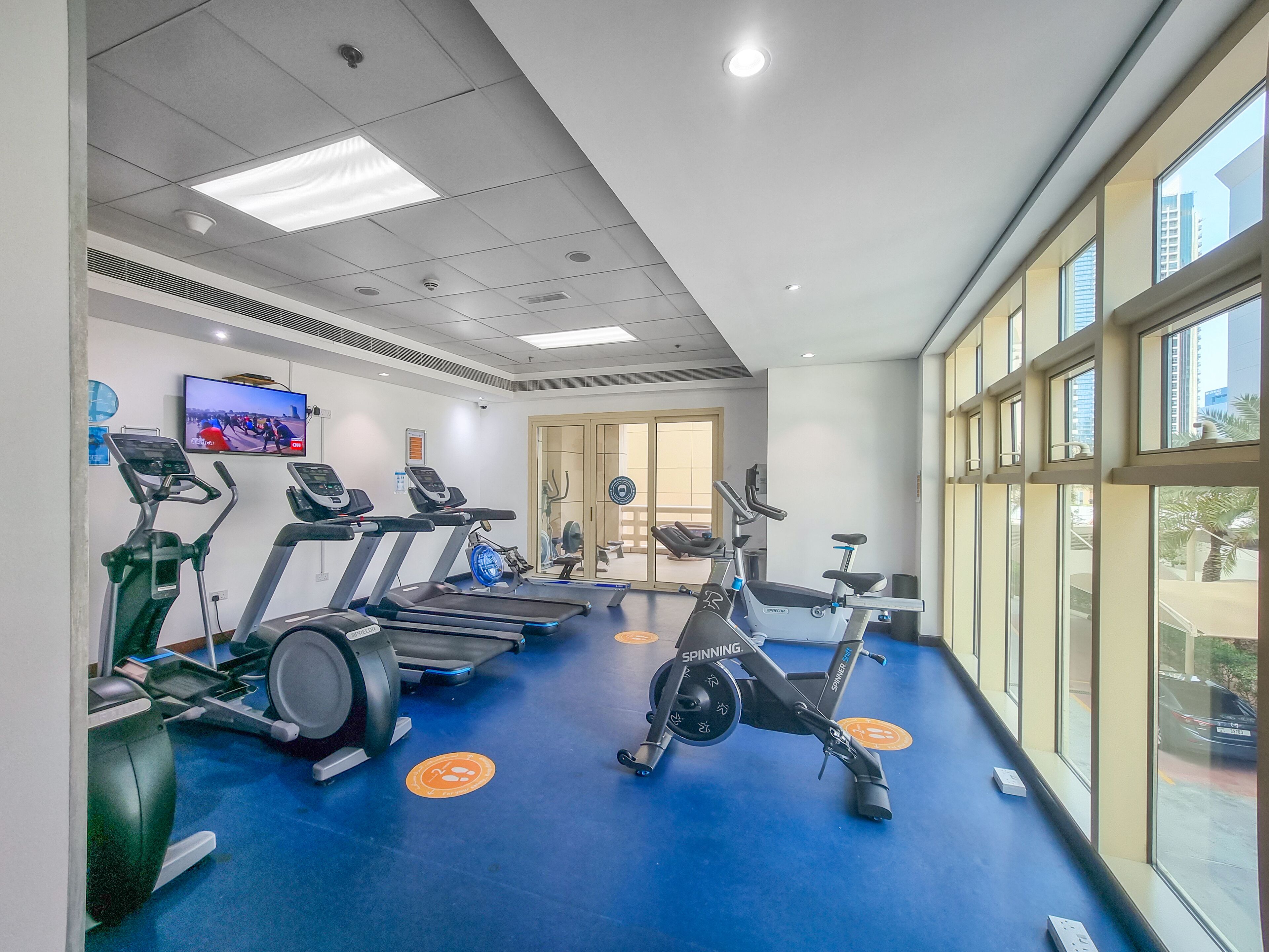 A gym with treadmills, stationary bikes, and a TV screen displaying a running event.