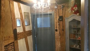 A hallway with wooden beams, a chandelier, a red rug, and a shelf with decorative items. - Romantic studio in renovated half-timbered house from 1706, with courtyard and garden (Bodman-Ludwigshafen)