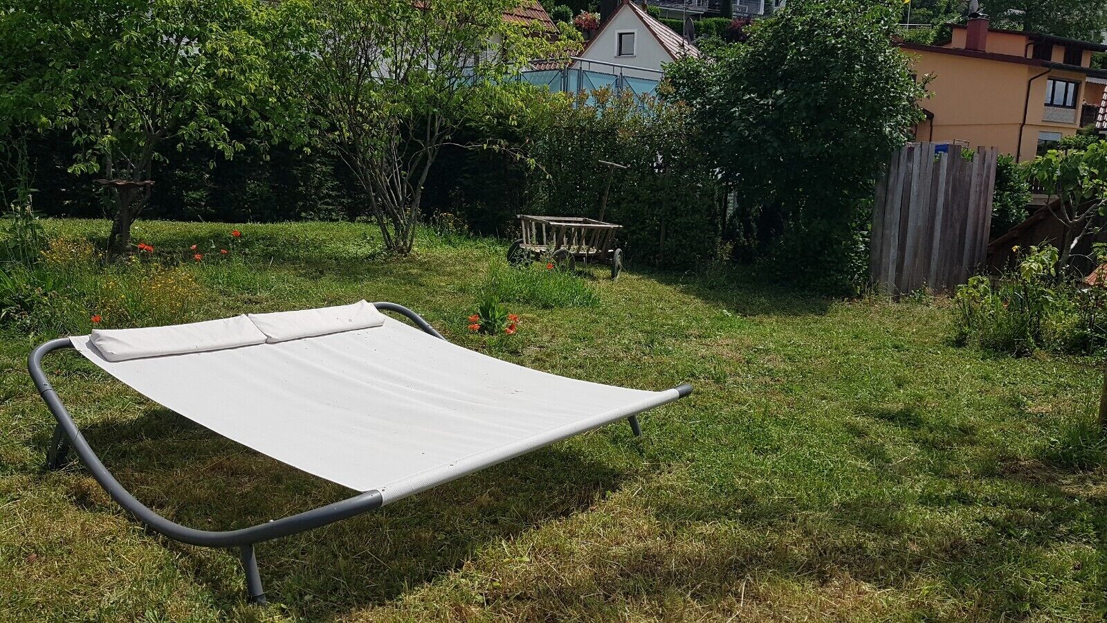 Una hamaca en un patio trasero con césped, árboles y una valla de madera.