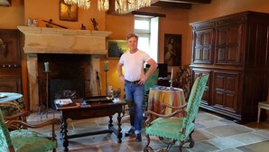 A man standing in a room with a fireplace, a green upholstered chair, and a wooden cabinet. - Romantic studio in renovated half-timbered house from 1706, with courtyard and garden (Bodman-Ludwigshafen)