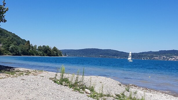 A lake with a sailboat, surrounded by a rocky shoreline and hills in the background. - Romantic studio in renovated half-timbered house from 1706, with courtyard and garden (Bodman-Ludwigshafen)