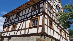A traditional half-timbered building with multiple windows and a stone base. - Romantic studio in renovated half-timbered house from 1706, with courtyard and garden (Bodman-Ludwigshafen)
