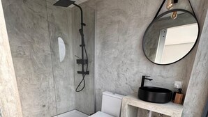 Ein modernes Badezimmer mit einer gläsernen Duschkabine, einer weißen Toilette und einem runden Spiegel über einem schwarzen Waschbecken.