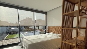 Ein modernes Schlafzimmer mit einem großen Bett, einer Holzhängeregalschrank und Blick auf einen Garten durch raumhohe Fenster.