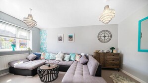 A modern living room with a sectional sofa, a round coffee table, and a wooden cabinet. - Spacious 3 bed House Garden Parking Wifi Smart tv (Coventry)