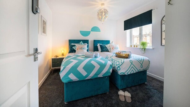 A bedroom with two beds, a nightstand, a lamp, a globe light, and a window with a view. - Spacious 3 bed House Garden Parking Wifi Smart tv (Coventry)