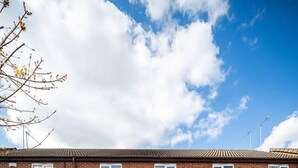 A two-story brick apartment building with a central entrance, satellite dishes, and a small garden area. - Spacious 3 bed House Garden Parking Wifi Smart tv (Coventry)