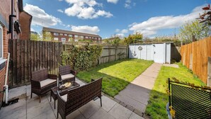 A backyard with a patio area, a wooden fence, a shed, and a grassy lawn. - Spacious 3 bed House Garden Parking Wifi Smart tv (Coventry)