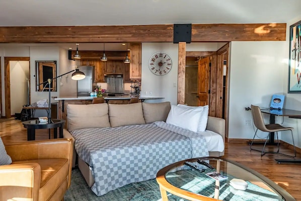 A cozy living room with a sofa, a glass coffee table, and a kitchen in the background.