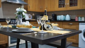 A kitchen with wooden cabinets, a black countertop, and a dining area with a table set for two. - Huge House Pool Table Parking Garden sky tv Wifi (Gloucester)