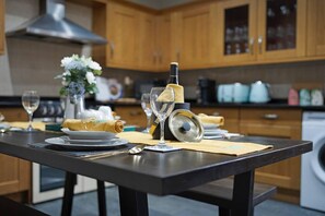 Uma cozinha com armários de madeira, bancada preta e um espaço de refeições com mesa posta para dois.
