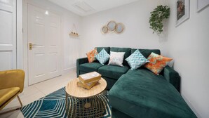 A living room with a green sofa, patterned cushions, a small wooden table, and a blue and white striped rug. - Lovely Little House, Free Parking, Smart tv, Wifi (Gloucester)