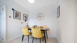 A dining area with a table set for four, yellow chairs, and a clock on the wall. - Lovely Little House, Free Parking, Smart tv, Wifi (Gloucester)