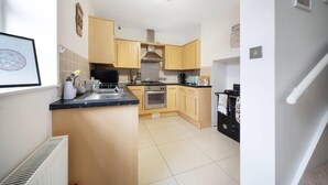 A modern kitchen with wooden cabinets, a built-in oven, and a black stove. - Lovely Little House, Free Parking, Smart tv, Wifi (Gloucester)
