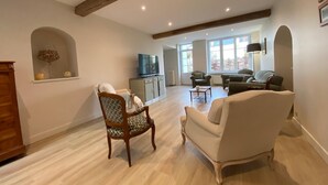 Ein geräumiges Wohnzimmer mit hohen Decken, Holzbalken, einem Fernseher und einer Sitzecke mit Sofa und Sesseln.