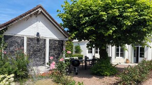 Ein weißes Gebäude mit einem Ziegeldach, ein Garten mit verschiedenen Pflanzen und Blumen sowie ein Tisch mit Stühlen draußen.