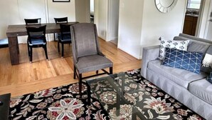 A living room with a sofa, a coffee table, a patterned rug, a dining area with chairs, and a wall-mounted mirror. - Sunny Hilltop 2-BR Top Floor in Arlington (Arlington)