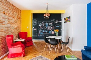 Un área de comedor con pared de pizarra, sillas rojas y una mesa blanca.