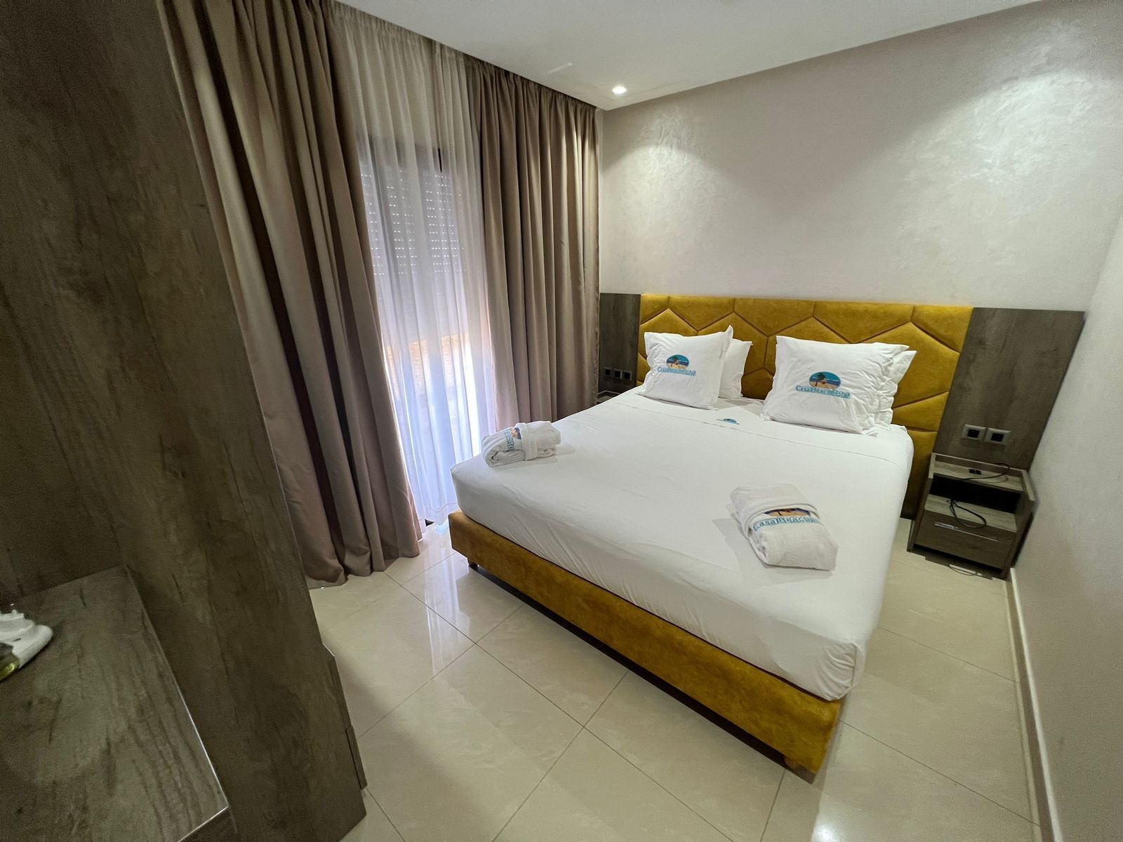 A hotel room with a large bed, a wooden headboard, and a nightstand with a lamp.