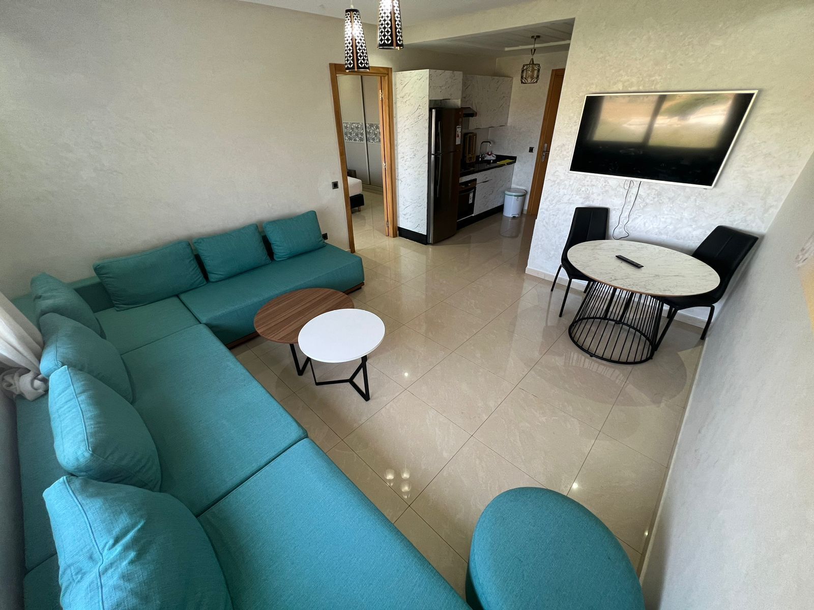 A modern living room with a teal sectional sofa, a round coffee table, and a dining area with a small table and chairs.