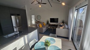 A modern kitchen with a built-in refrigerator, a dining area with a table and chairs, a sofa, and a TV in the living area. - Pickleball Dream - All New, Modern Condo in Sea Colony. 10mins walk to the beach (South Bethany)