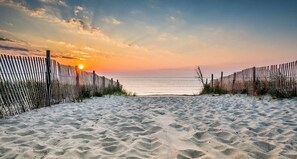 A sandy beach with a wooden fence and a sunset in the background. - Pickleball Dream - All New, Modern Condo in Sea Colony. 10mins walk to the beach (South Bethany)