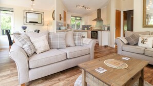A spacious living room with a beige sofa, a wooden coffee table, and a kitchen in the background. - Nutkins Lodge (Windermere)