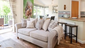 A cozy living room with a sofa, a dining table, and a kitchen area. - Nutkins Lodge (Windermere)