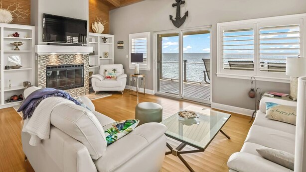 A spacious living room with a fireplace, comfortable seating, a television, and a view of the ocean through large sliding doors. - Just Like Heaven - Beachfront (Crawfordville)