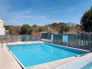 A rectangular swimming pool with a tiled deck, surrounded by a wooden fence.