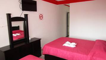 Habitación de hotel con dos camas, televisión, ventilador de techo y cartel de no fumar.